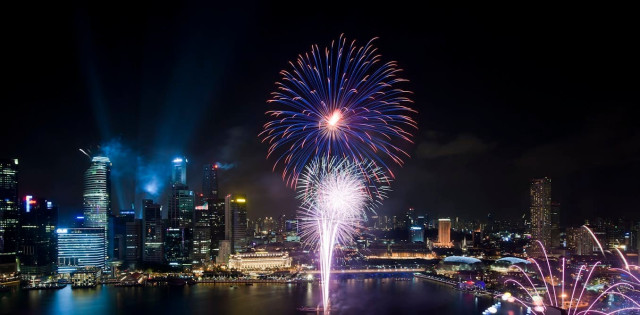 Fireworks exploding over a city harbor.
