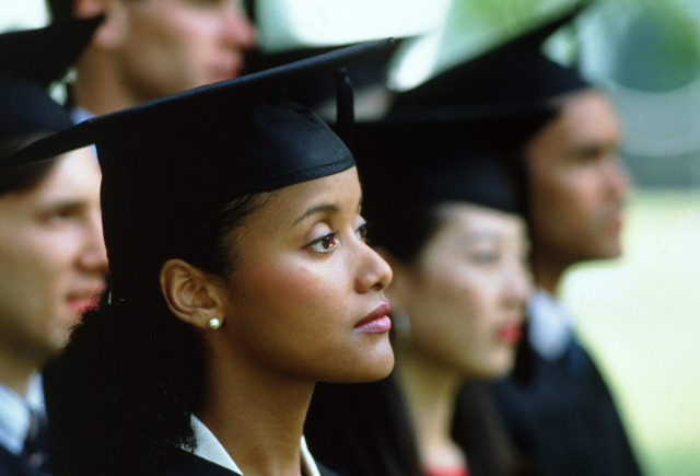 A woman with a look of uncertainty wears a black graduation cap.