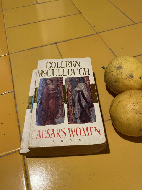Colleen McCullough’s book Caesar’s Women in an old and very worn paperback edition, two lemons photobombing 