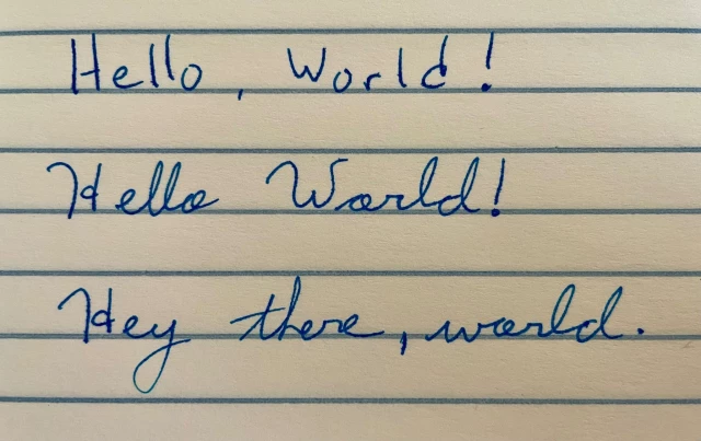 Handwritten note in blue ink on yellow paper with blue ruled lines. 

"Hello, World!"  -- printed
"Hello World!" -- cursive
"Hey there, world." -- also cursive