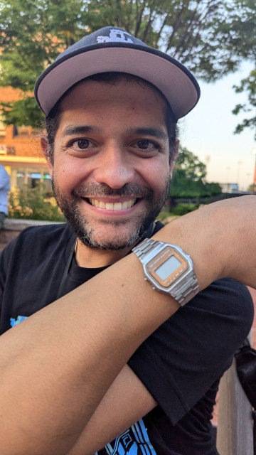 Close up shot of a smiling Joey showing off his silver Casio watch. The face of the watch is blank