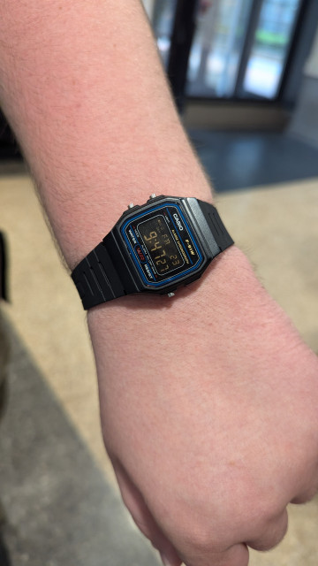 Close up shot of an arm wearing a Casio f91w wrist watch. The screen is inverted in colour, so the time is white and the background is black.