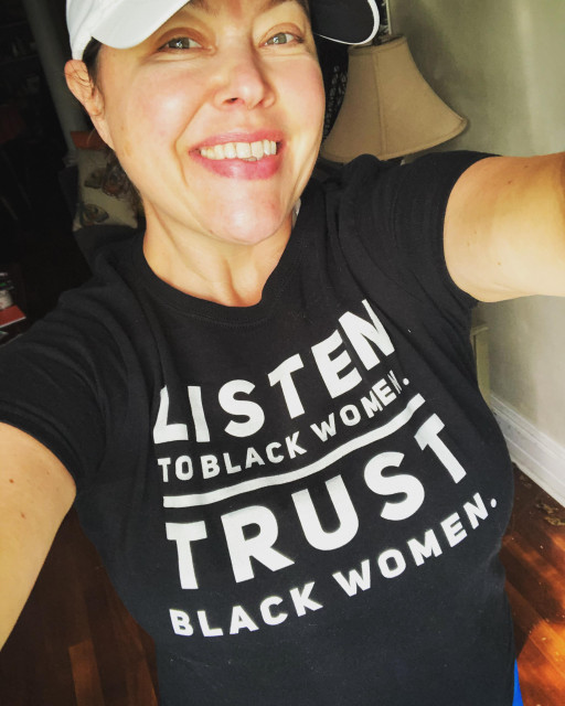 A selfie of me. I am wearing a black tee shirt with white lettering that says, “Listen to Black women. Trust Black women.”