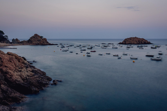 Vista durante el atardecer de la playa y costa de parte de Tossa de Mar con algunas barcas en el mar.