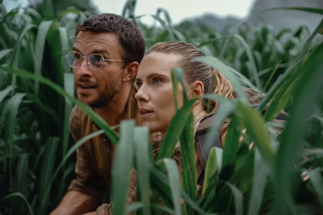 Still from Jurassic World Rebirth, Jonathan Bailey and Scarlett Johansson are in a corn field looking at something out of the picture