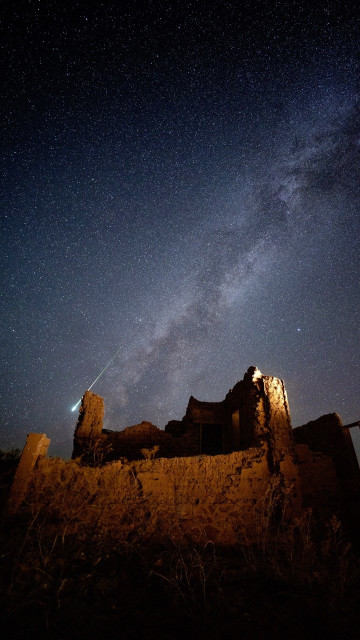 A glowing green meteor flying behind the ruins of an old building