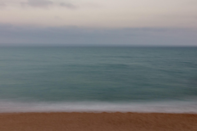 Fotografía usando larga exposición y moviendo ligeramente la cámara donde se ve el mar en una gran franja central y en la parte inferior, algo de tierra de la playa mientras en la superior un algo del cielo difuminado.