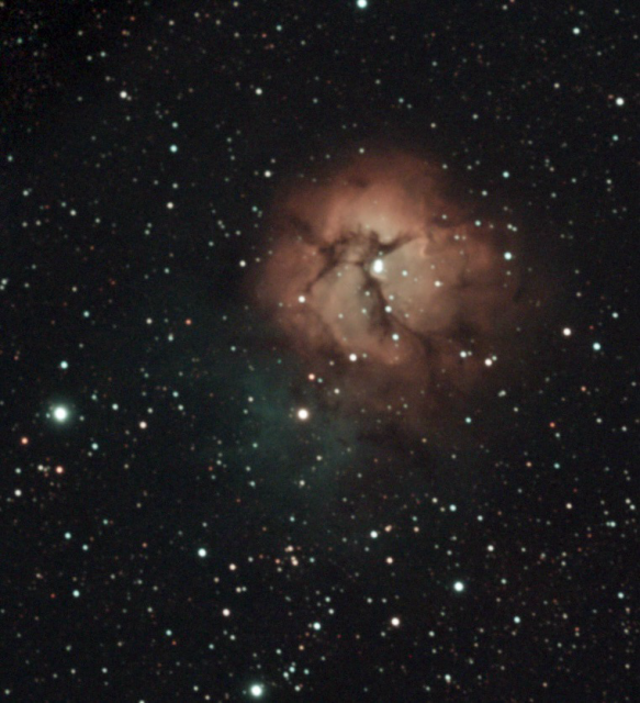 A dense star field surrounds a bright, multi-coloured nebula. One region of the nebula is reddish in colour. This is the hydrogen gas that has been excited by the hot massive stars at the centre of the nebula, causing it to be ionised. This structure is also crossed by dark dust lanes, in an x-shape. These are the dark nebula which are silhouetted against the red portion of the nebula. To the lower left are faint hues of blue-green gas. This is the dust that is reflecting light in our direction.