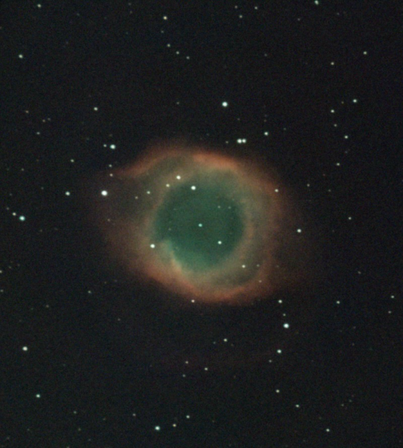 A central, large ring-like nebula. The inner part of the ring is a blue-green colour and is diffuse, whilst the outer ring region is reddish in hue, much more defined and clumpy. A central small white star, the white dwarf, emits powerful UV radiation which excites the different elements producing different colours. Surrounding the nebula are many stars.