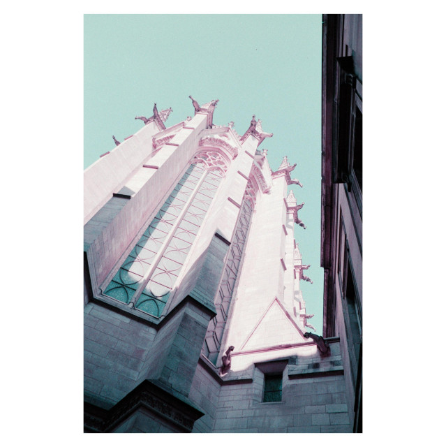 Sainte-Chapelle, Paris. The view is from a shady corner outside the chapel, looking up at the gargoyles perched high enough to escape the shade. The film has cast the stone a light purple and the clear sky slightly turquoise.