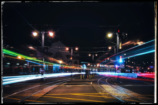 Taken at night, the lights from two MUNI streetcars streak past on either side of a median divider on San Francisco's Embarcadero roadway. 

The colorful lights on the right, red and blue, are from a streetcar headed towards Oracle stadium. The green and blue lights in the left are from an inbound streetcar headed towards Market Street. 

I was lucky to be there when the cars crossed in both directions at the same time.