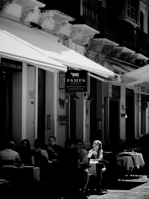 Street scene from Málaga's historic centre where a woman is picked out in a brilliant shaft of light while all those around her are cast into shadows outside a restaurant.