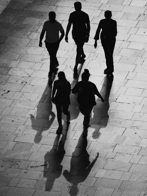 Low, late evening sunlight throws five people into shadow as they walk in a three-two formation across a bridge in central Málaga