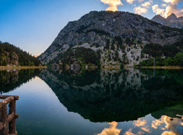 Fotografía del ibón de los baños (Panticosa). Se trata de una panorámica de tres fotos donde se ve parte del ibón con algunas de las montañas que los rodean al atardecer. Se refleja el paisaje en las aguas del ibón.