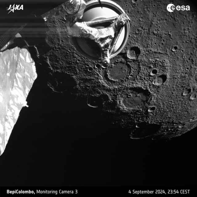 A black-and-white picture of part of the planet Mercury showing lots of craters and other surface features, seen against a black sky with some parts of the ESA/JAXA BepiColombo spacecraft in the foreground.