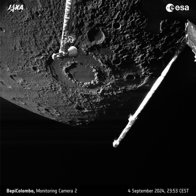 A black-and-white picture of part of the planet Mercury showing lots of craters and other surface features, seen against a black sky with some parts of the ESA/JAXA BepiColombo spacecraft in the foreground.