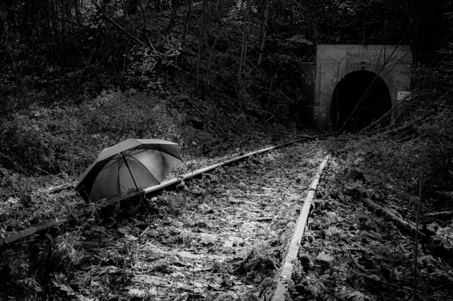 Ein Schwarz-Weiß-Foto eines verlaubten Gleisbetts kurz vor einem Tunnel. Auf dem linken Gleis liegt ein aufgespannter Regenschirm. 