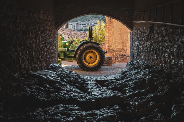 Se ve un paso techado callejero en Alquézar (Huesca) con un suelo irregular de piedra. Al final se ve un pequeño tractor.