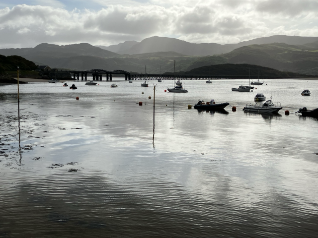 Amazing light makes the water look like rippled mercury; the moored boats are dark silhouettes, as the railway bridge in the distance. The mountains behind fade in shades of green-grey and almost the only thing revealing this image is not black and white is the patch of pale blue in the sky, reflected on the silver mirror of the water.