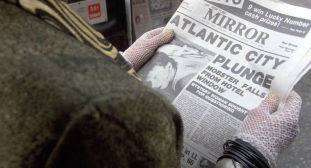 A woman holding a newspaper dated September 11, 1984. The headline is “Mobster falls from hotel window”