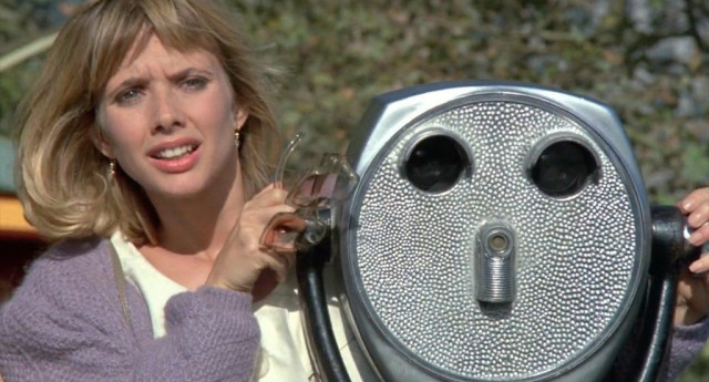 A woman in a preppy sweater peers out from behind a pair of street binoculars