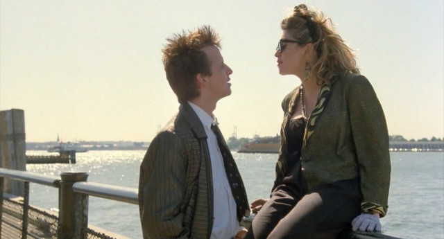 A man and woman chat next to a river in New York. The woman, played by Madonna, is sitting on the railing