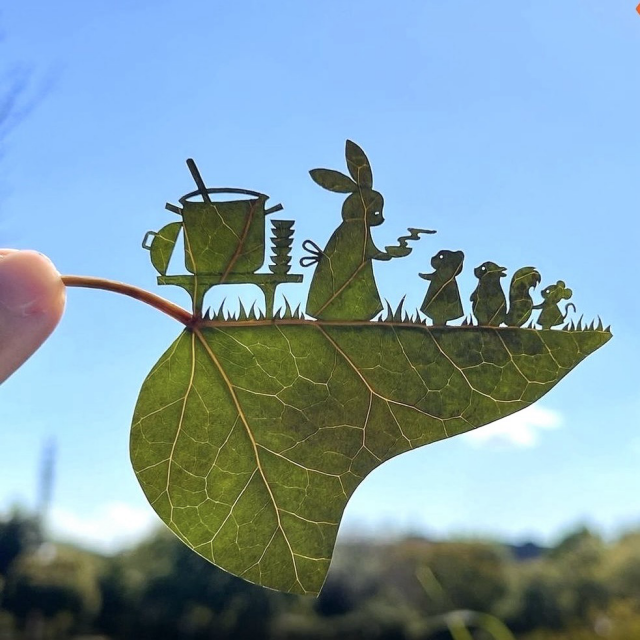 Cut-out leave which depicts a mother rabbit cooking food for her young who are standing in a line & waiting to be served. The pot is on the side & boiling.