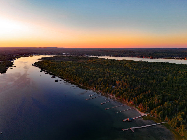 A red sunset lines the horizon above the extensive green forest and blue waters of northern Michigan. Rows of homes and docks can be seen from this arial photo looking west across an island in Lake Huron.