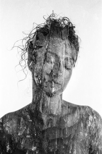 A woman's upper torso and face. She has her eyes closed and her hair drawn loosely above her head. The rocky texture from the double exposure gives the feel of a crumbling statue to the whole image. Black and white. 