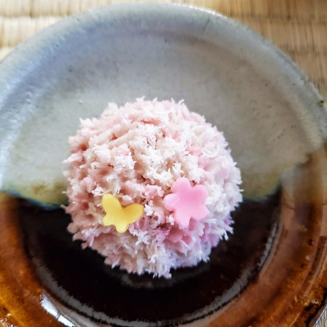 A delicate pink kinton sweet is decorated with a tiny yellow butterfly and sakura blossom.