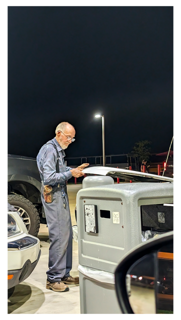 night at the circle k. an elder man holds the hood of his white pickup and is looking down. the front tip of a white SUV behind him. the front tip of a gray, jacked-up pickup in the next fuel bay immediately behind. a streetlight in the distance under a black night sky.