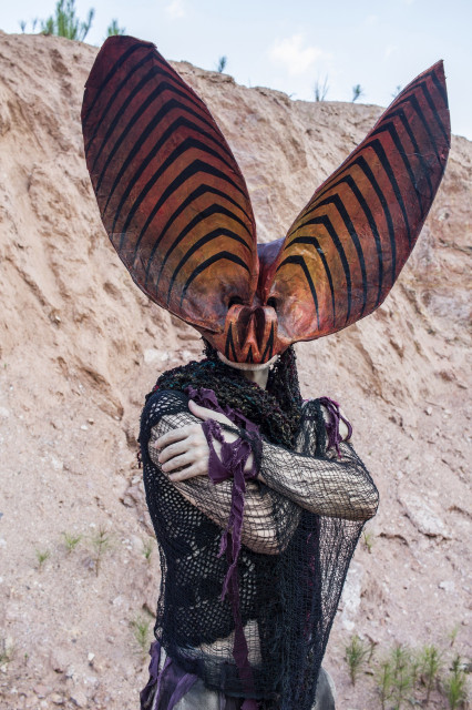 a portrait of a person wearing an ornate papier mache bat mask with huge striped ears