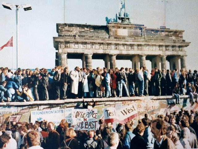 Germans stand on top of the Wall in front of the Brandenburg Gate.