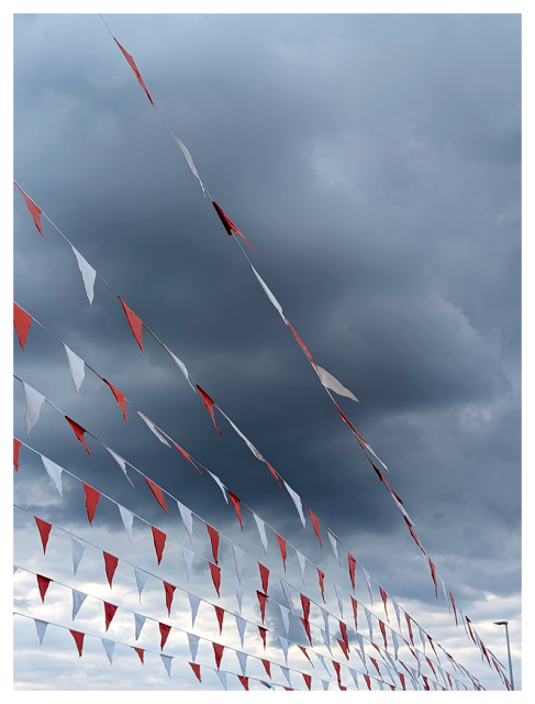 storm-cloudy afternoon. 8 parallel strings of orange and white pennant flags stretch from the left side of the picture down to bottom right.