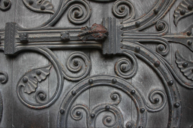 close up view of an old solid wood door. the metal handle stretches across the middle and breaks out into vine scrolling and leaves