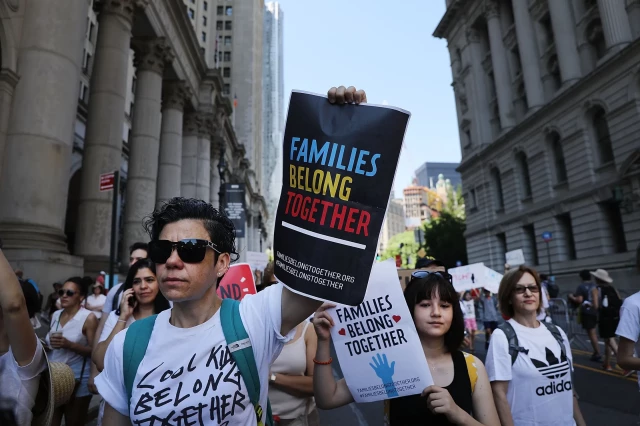 Image of people protesting family separation.  A protester holds up a sign reading, "Families Belong Together."