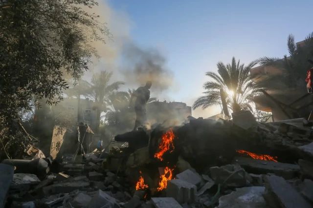 A man climbs on a smoking, burning pile of rubble 