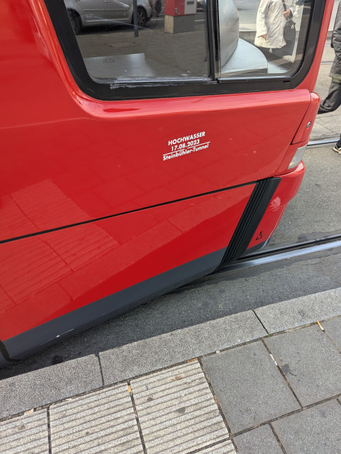 Die Spitze der VAG Straßenbahn 1115 (Typ: CityBahn GT8N) mit einer aufgeklebten Hochwasser Marke auf etwa Höhe von ca. 75 cm über dem Boden, sie liest: "Hochwasser 17.08.2023 Steinbühler Tunnel"