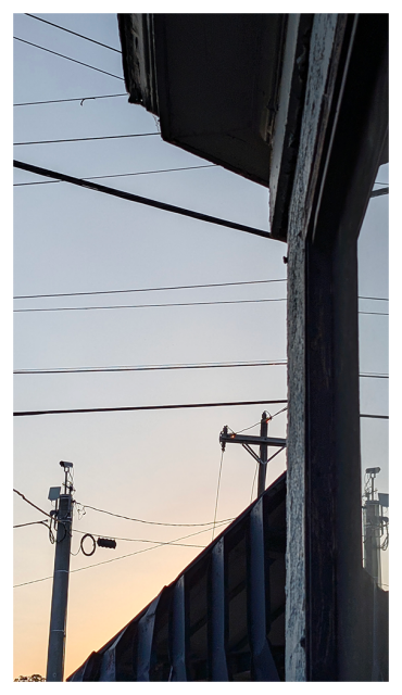 abstract at sunset. a reflective shop window, part of an awning over an unseen door, building eaves and power poles and line in the near distance. the background is pale gray sky with a hit of pale orange at bottom.