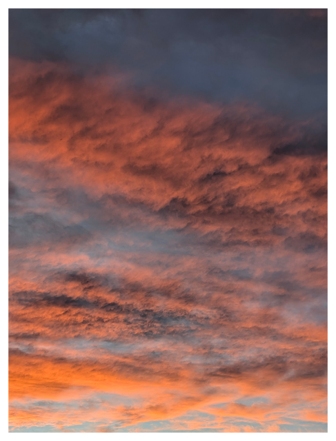 portion of the Western sky above the horizon at sunset, horizontal  bands of orange clouds with gray overlays. the sky behind is bright light blue.