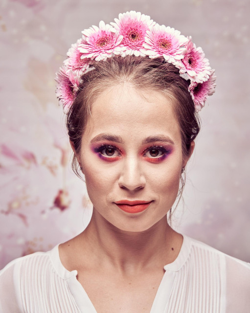 A woman in a pink gerbera headdress against a blossom background.