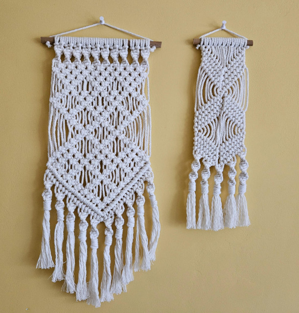 Two white macrame wall hangings against a yellow wall, one is large with complex diamond patterns, the other is smaller with a more minimal criss-cross design. 