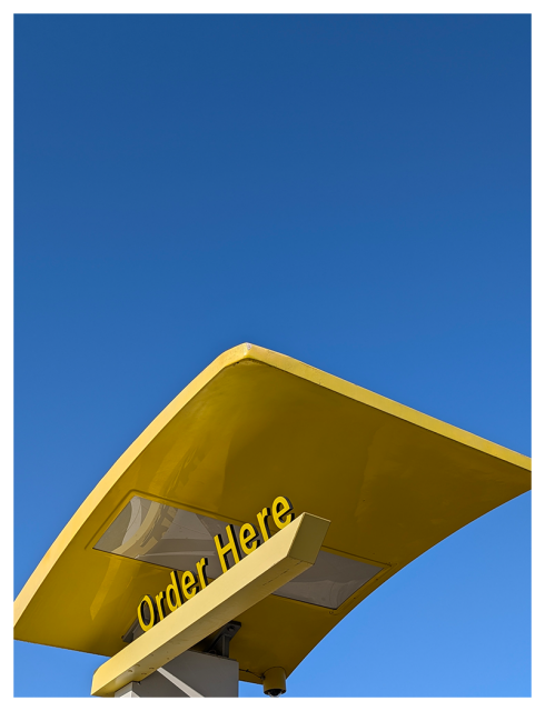 low-angle side view. the yellow canopy over the ORDER HERE spot in a mcdonald's drive-thru. the background is clear blue sky.