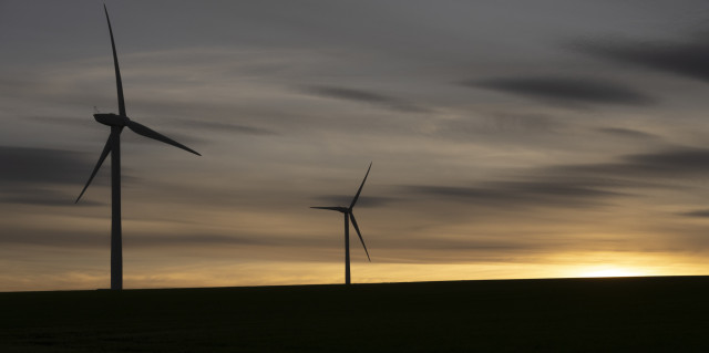 Two wind turbines are silhouetted by the setting sun to the right of the frame.