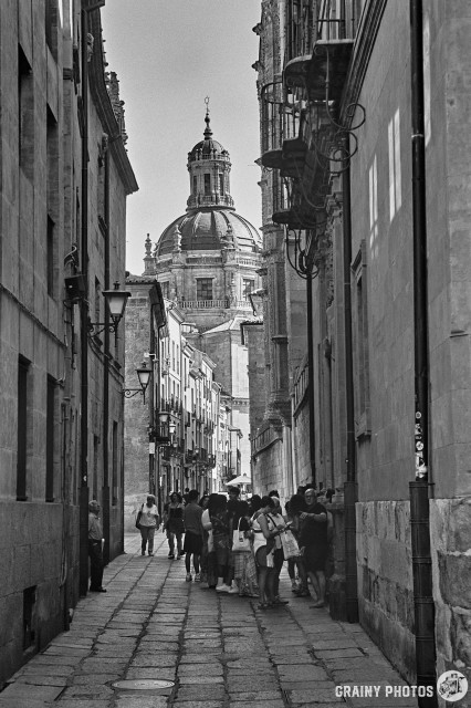 A black-and-white film photo of a narrow street in Santa Monica. In the distance is the tower of the university.