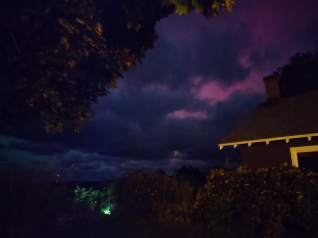 Photograph of clouds backlit by pinkish Aurora Borealis