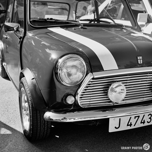 A black-and-white film photo of a mini. The photograph is of the front of the car, a three-quarter width view. The car has flared arches and a white stripe on the bonnet.