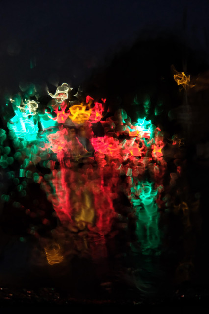 Photograph taken from inside a car showing the refraction of traffic lights caused by heavy rain on the windscreen, creating an abstract pattern in red, amber and green.