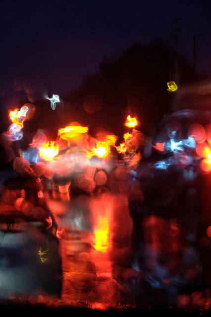 Photograph taken from inside a car showing the refraction of traffic lights caused by heavy rain on the windscreen, creating an abstract pattern in red and amber.