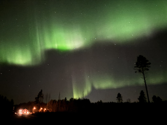 Two lines of aurora above a red wooden house in the countryside 